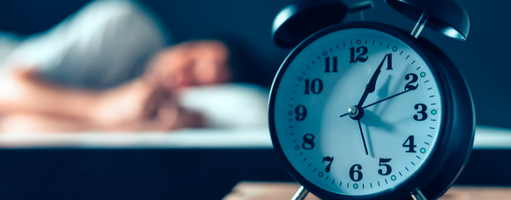 Alarm clock on bedside table with someone sleeping in the background