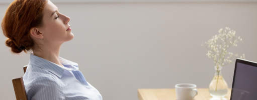 Woman leaning back on chair with eyes closed while sitting in front of a laptop